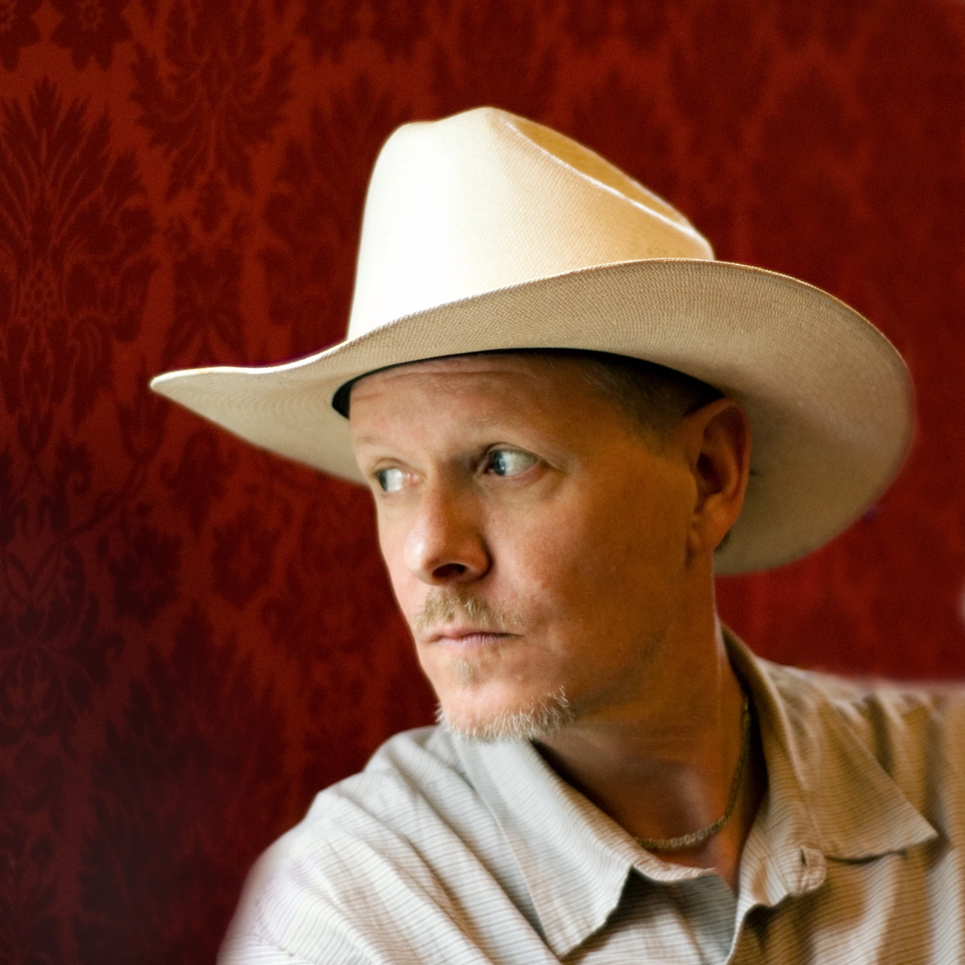 A portrait of a man wearing a light-coloured hat against a red background