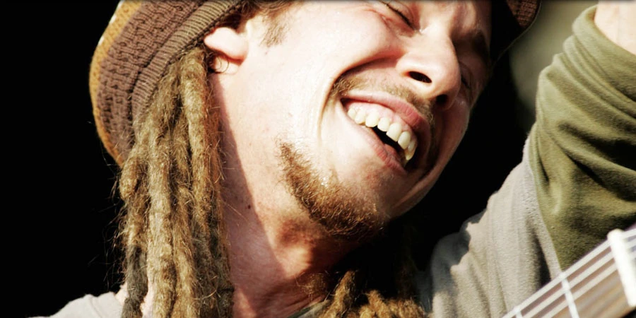 A close-up of a smiling Jahcoustix with a guitar