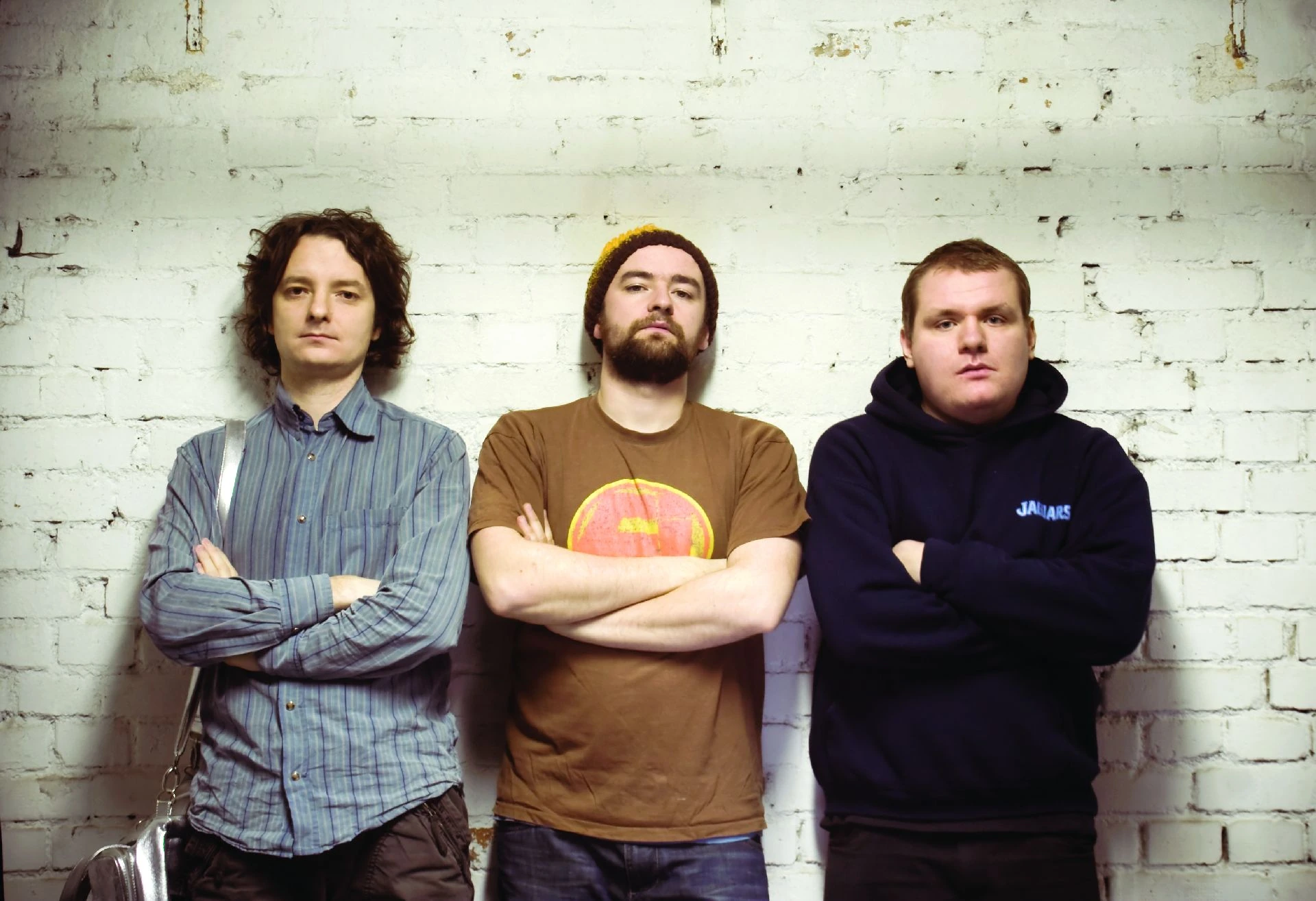 Three musicians standing in front of a light brick wall