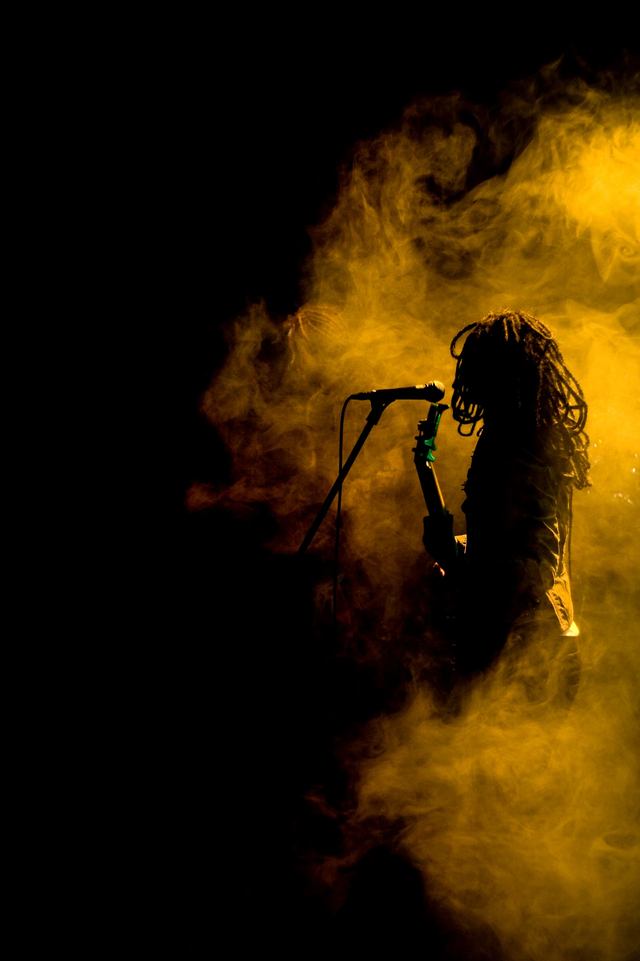 A singer silhouetted at a microphone in yellow stage smoke