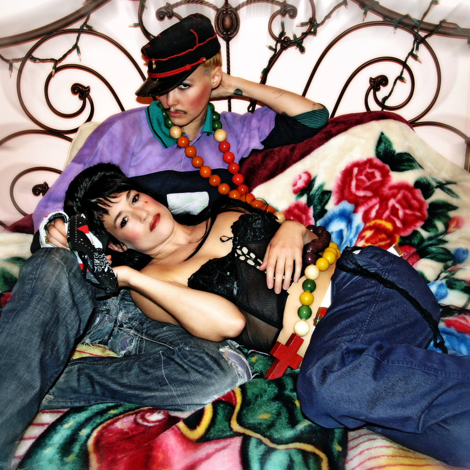 Siostry CocoRosie w barwnych strojach na łóżku z ozdobnym zagłówkiem