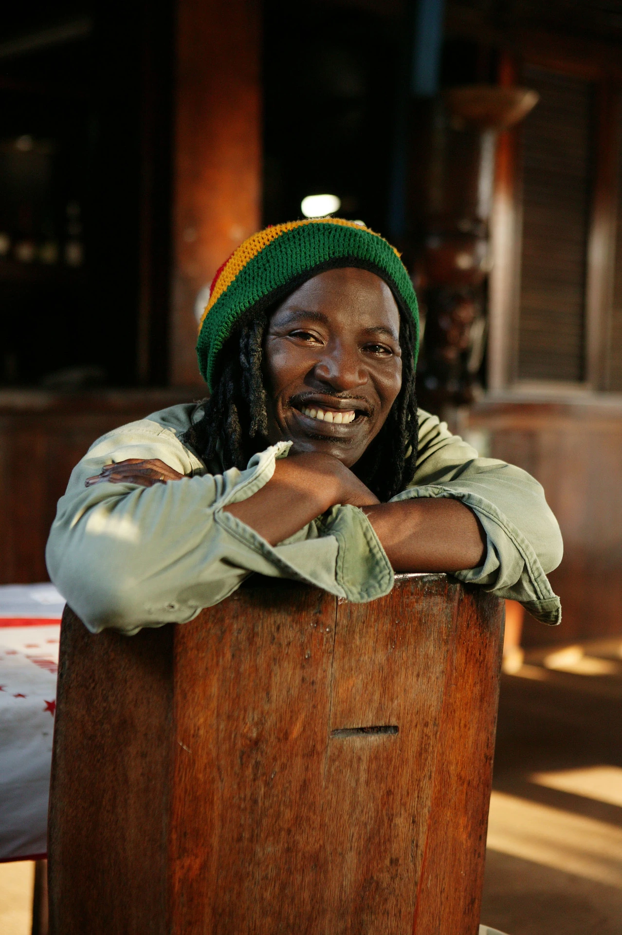Alpha Blondy wearing a green hat and resting on the back of a wooden chair
