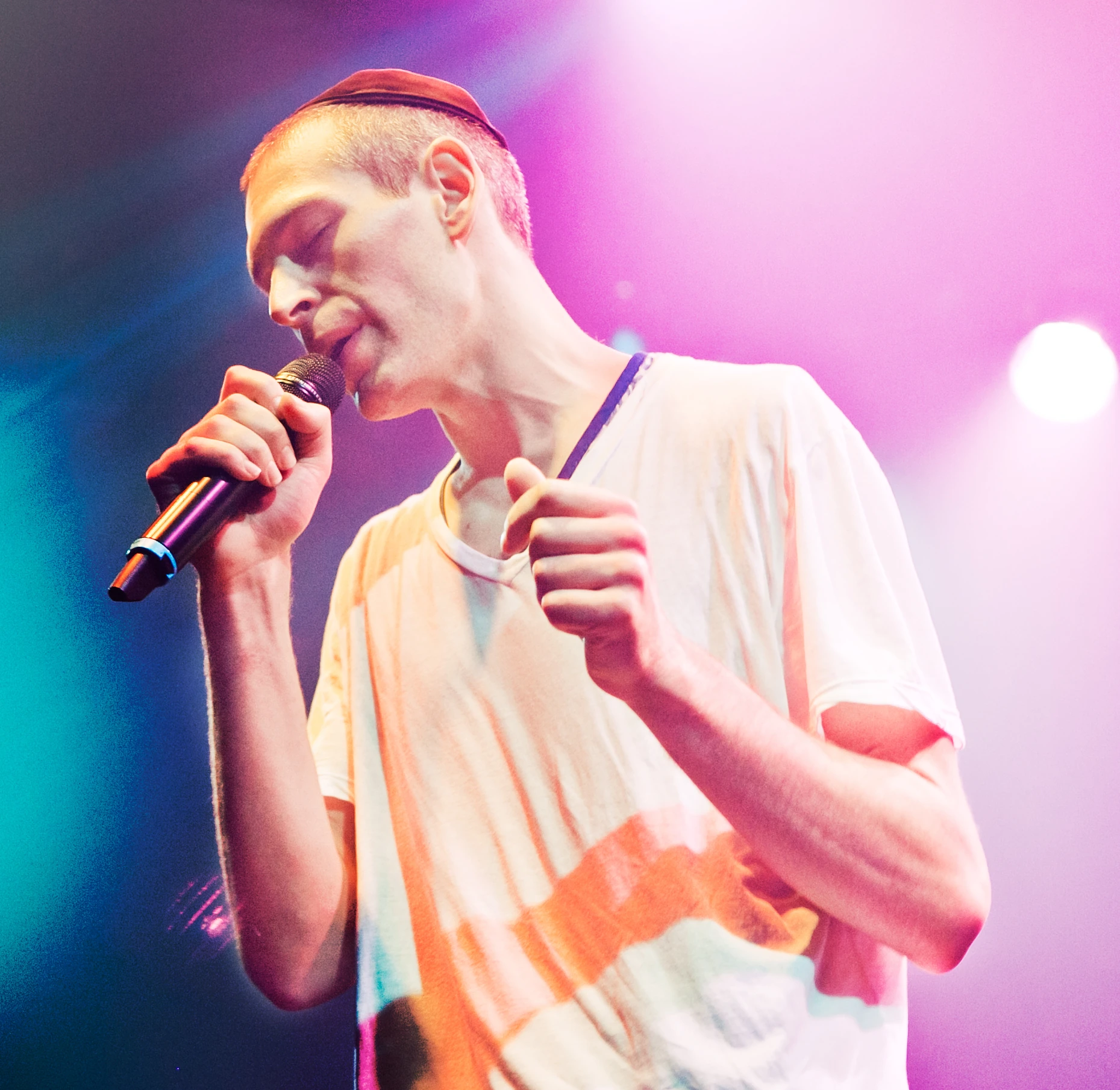 Matisyahu z mikrofonem podczas występu w kolorowym świetle
