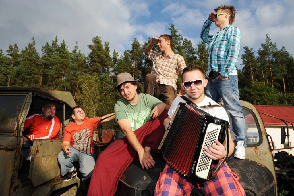 Enej musicians beside a car, with an accordion in the foreground