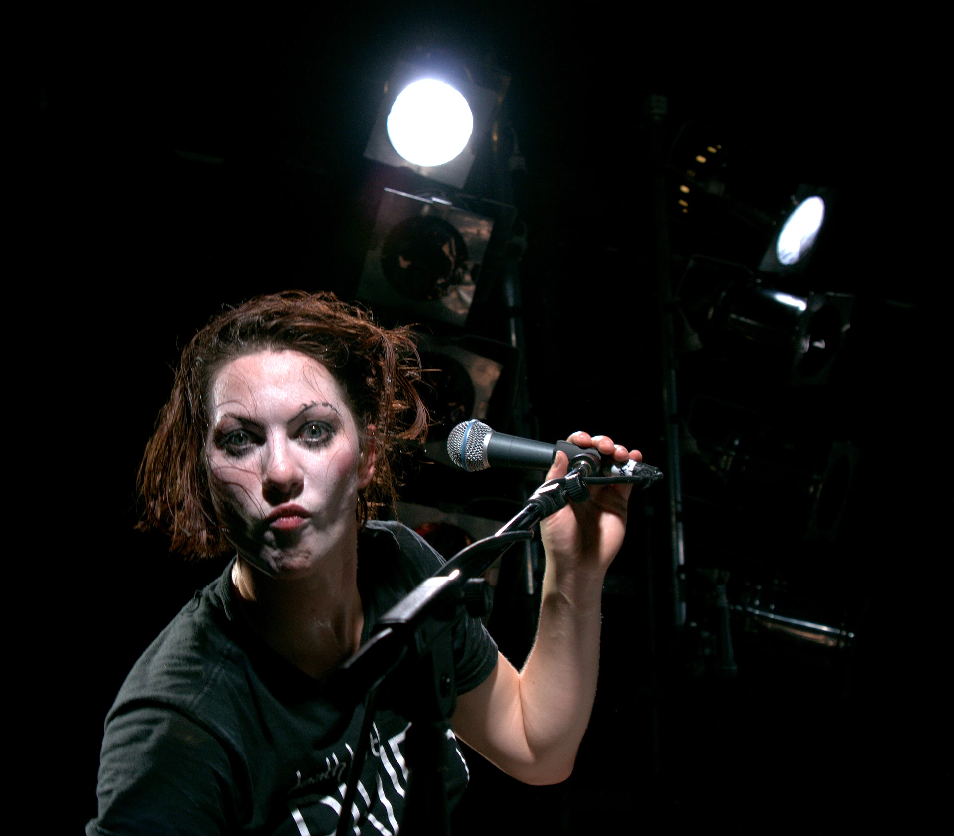 Amanda Palmer holding a microphone during a performance on a dark stage