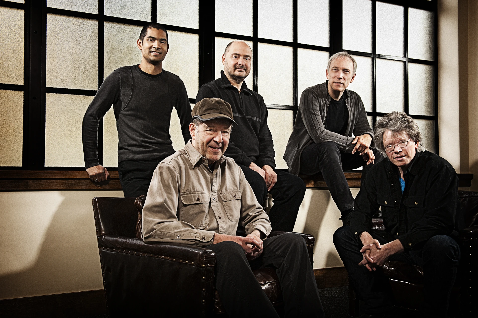 Five musicians posing beside chairs in a light interior