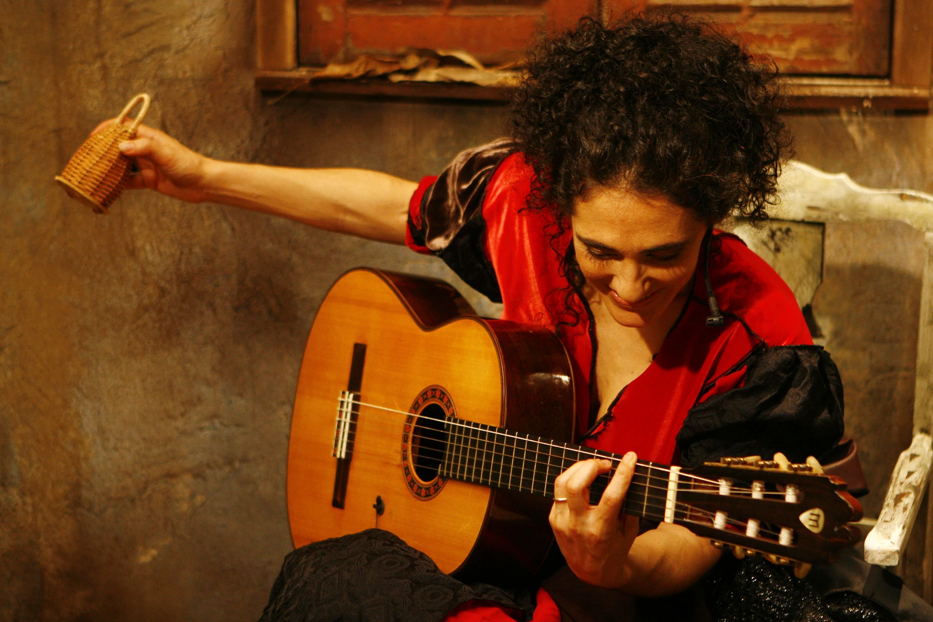 Badi Assad z gitarą akustyczną na tle kamiennej ściany
