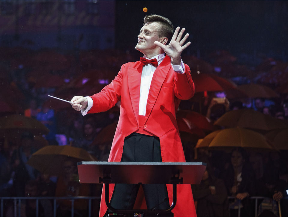 Mariusz Dziubek w czerwonym fraku dyryguje orkiestrą